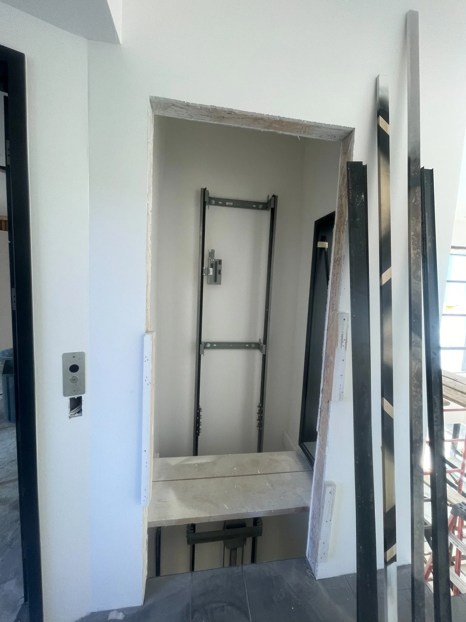 Construction site showing an elevator shaft frame with construction materials and tools around.