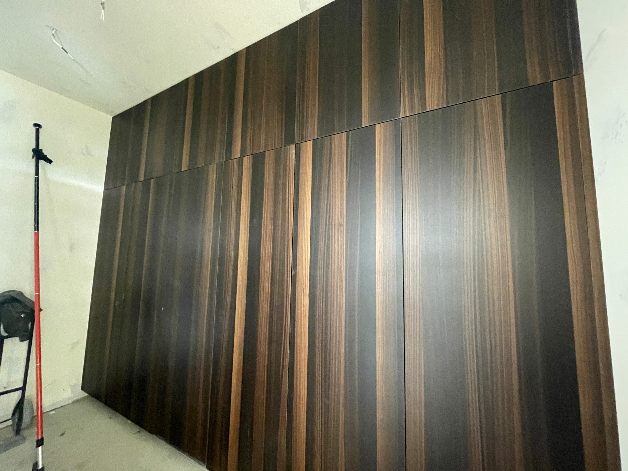 Large wooden cabinet with vertical panels, situated against a wall in a room under construction.