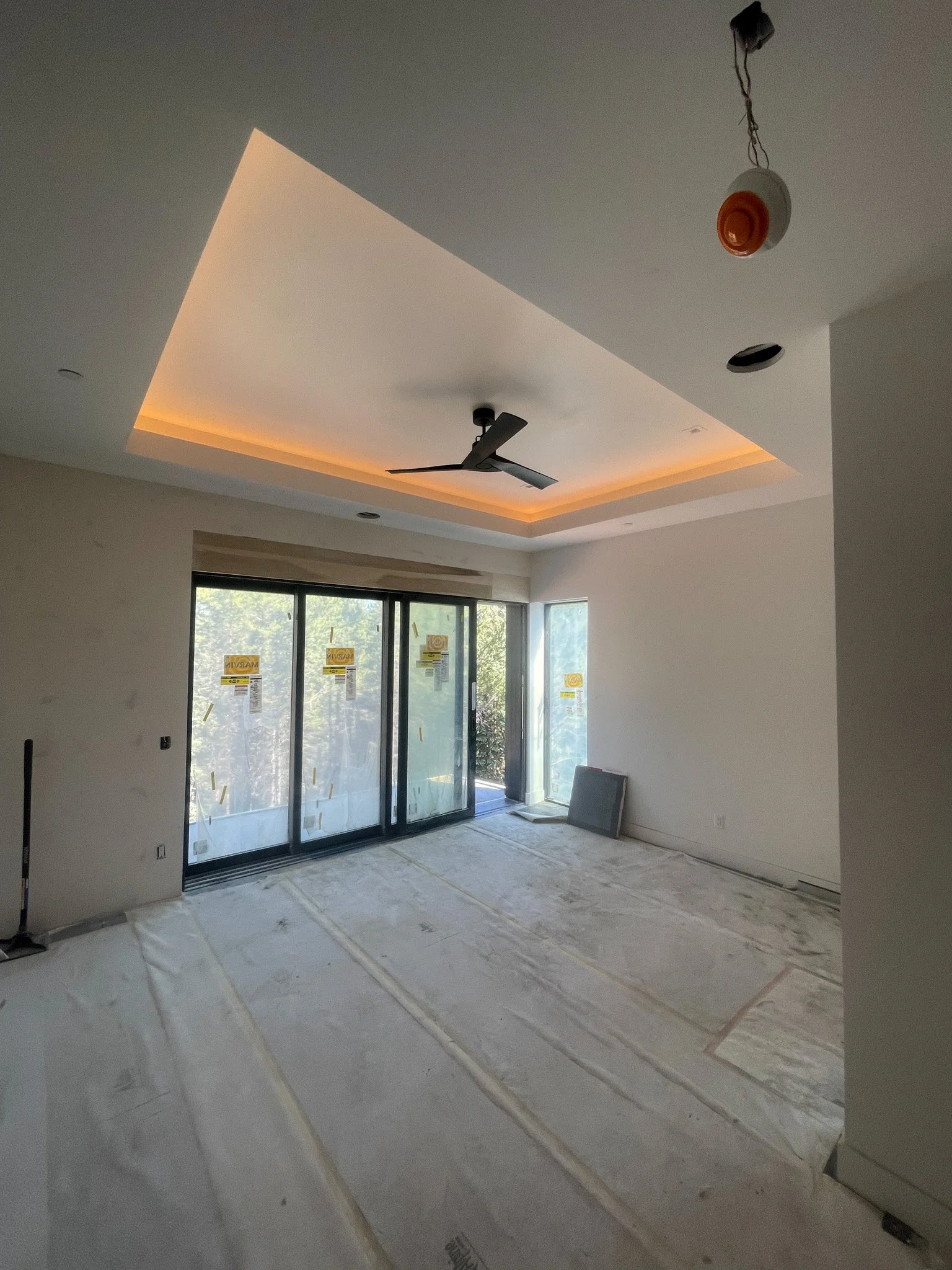 Empty room under construction with large sliding glass doors, a ceiling fan, recessed lighting, and an unfinished ceiling with a hanging light socket.