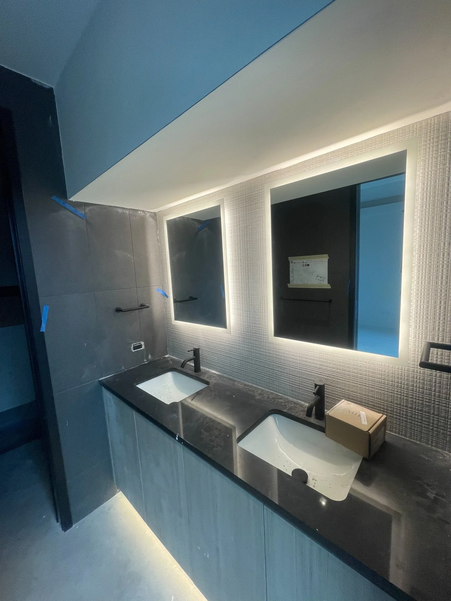 Modern bathroom with dual sinks, illuminated mirrors, and textured wall tiles.