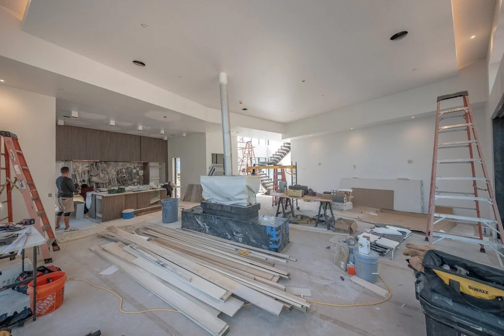 Interior of a house under construction with ladders, construction tools, and materials scattered around.