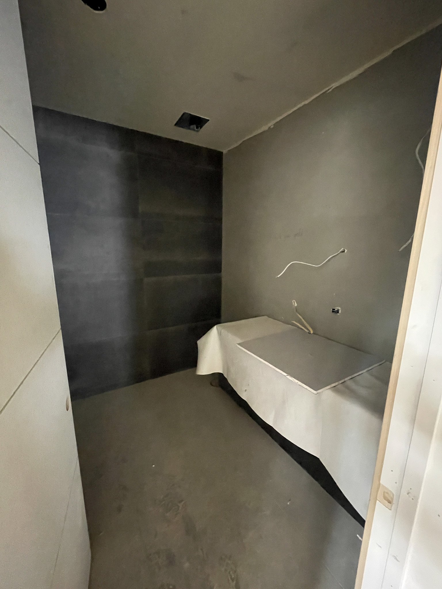 Room under construction with dark wall tiles, unfinished walls, and electrical wires visible.