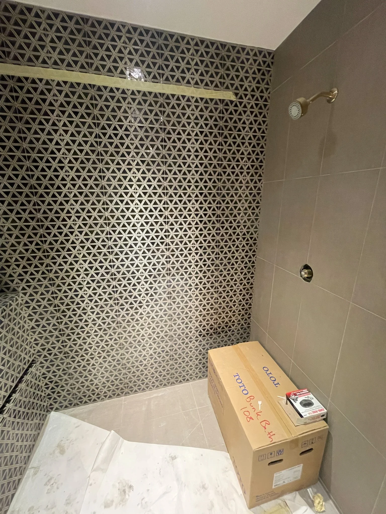 Bathroom with patterned tile wall, showerhead, and a cardboard box on the floor.