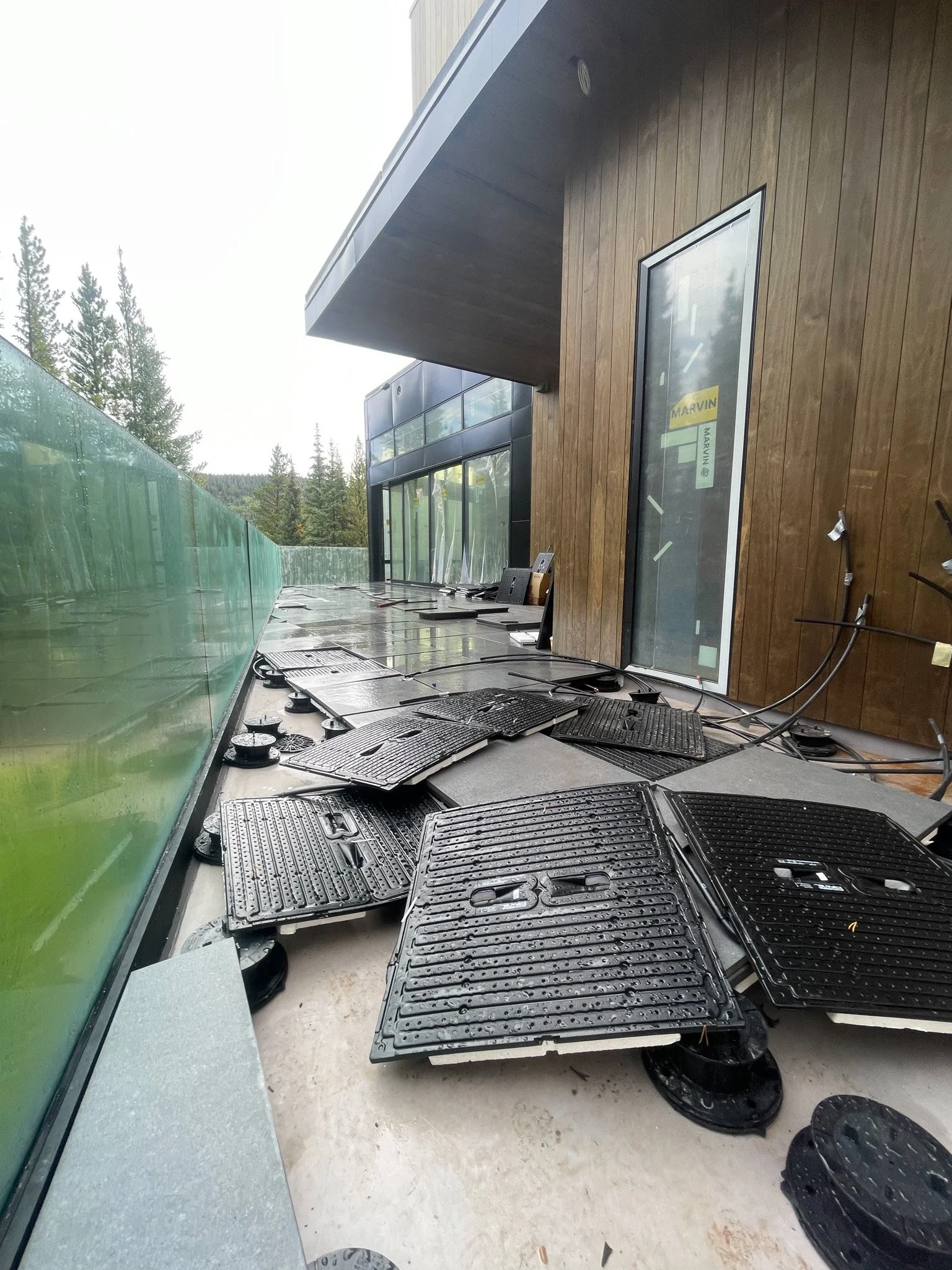 Construction site with scattered black electrical heater bases outside a modern building with wooden and glass exterior.