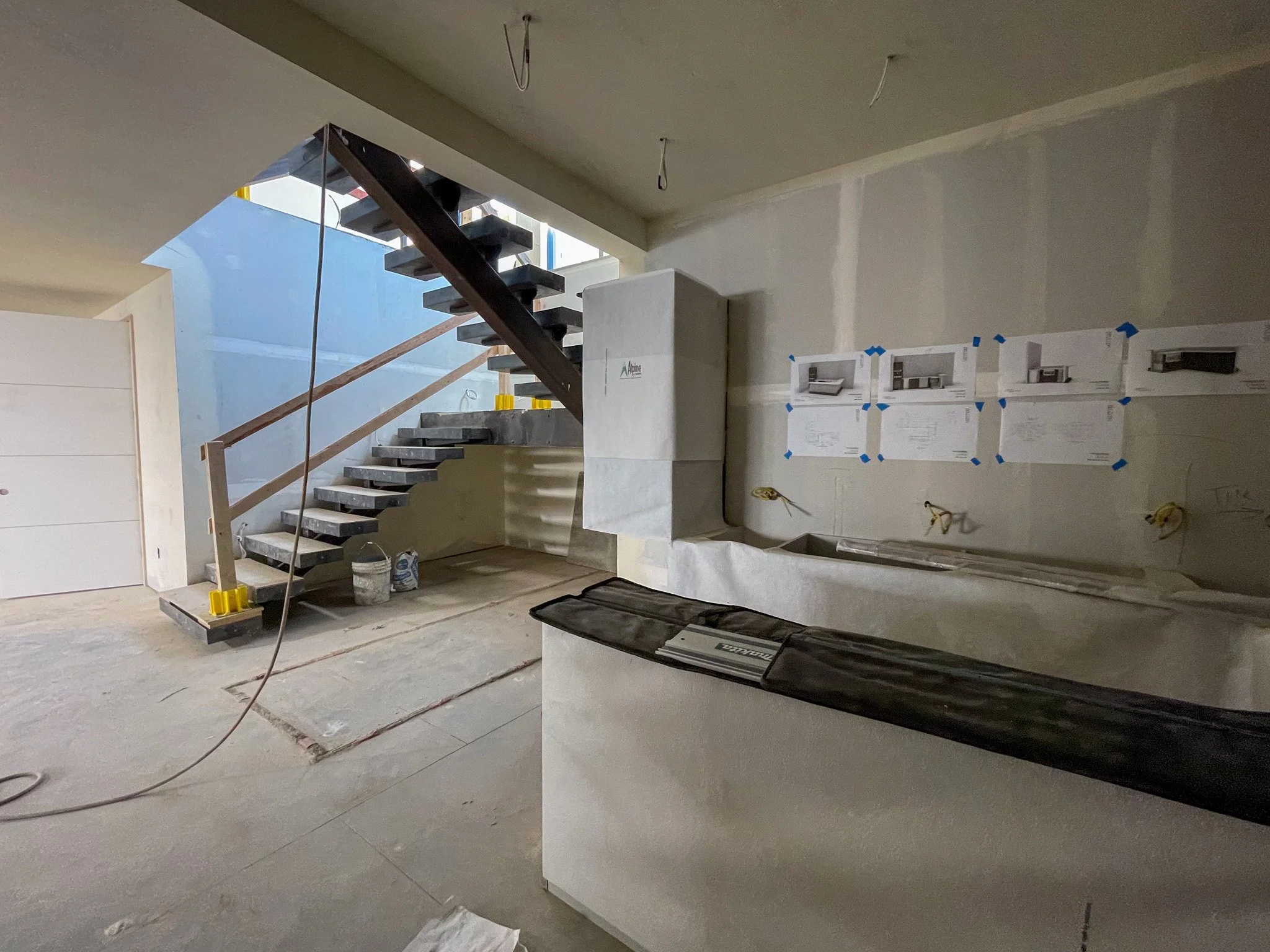Interior of a house under construction with stairs, construction materials, and blueprints on the wall.