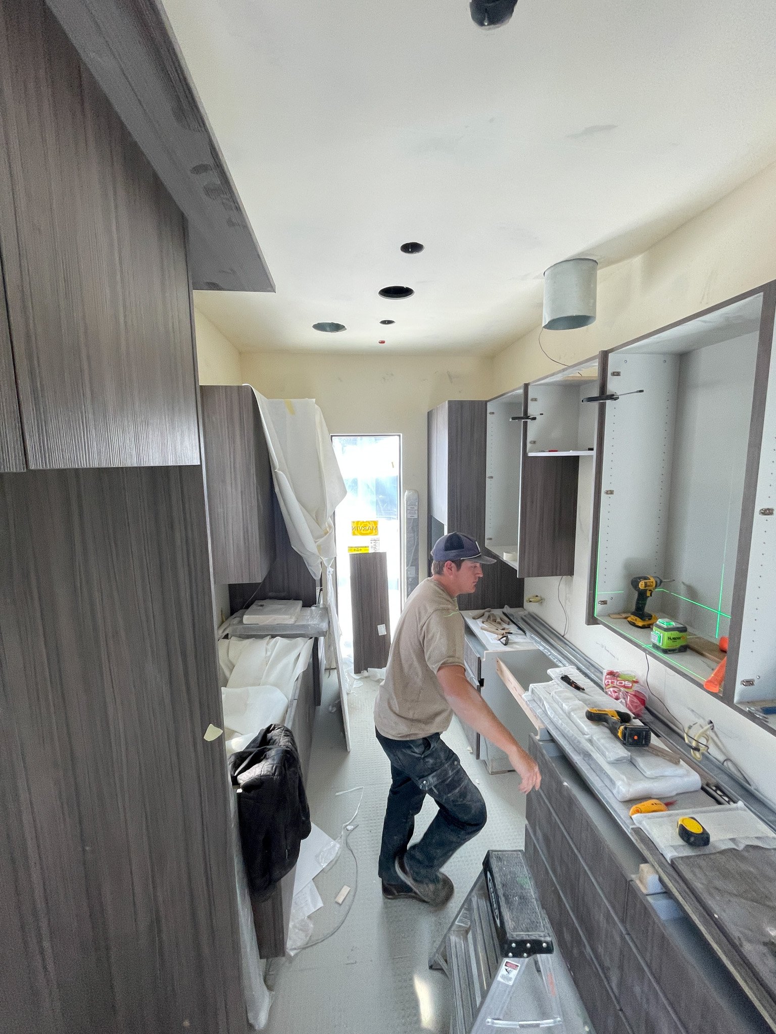A construction worker installing kitchen cabinets in a partially finished kitchen under renovation.