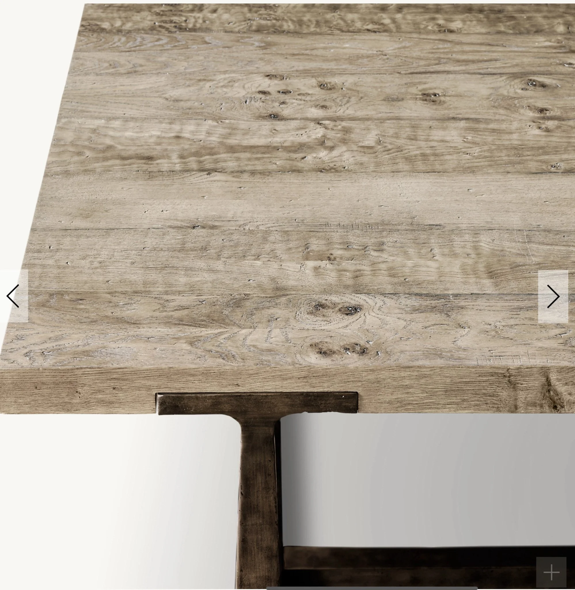 Close-up of a wooden table with a natural finish showing wood grain and knots, with a dark wooden leg visible beneath.