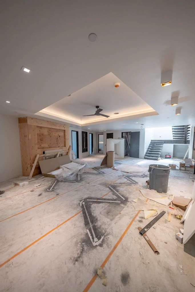 Interior of a house under construction, with unfinished flooring, construction materials, debris, and stairs leading to another level.