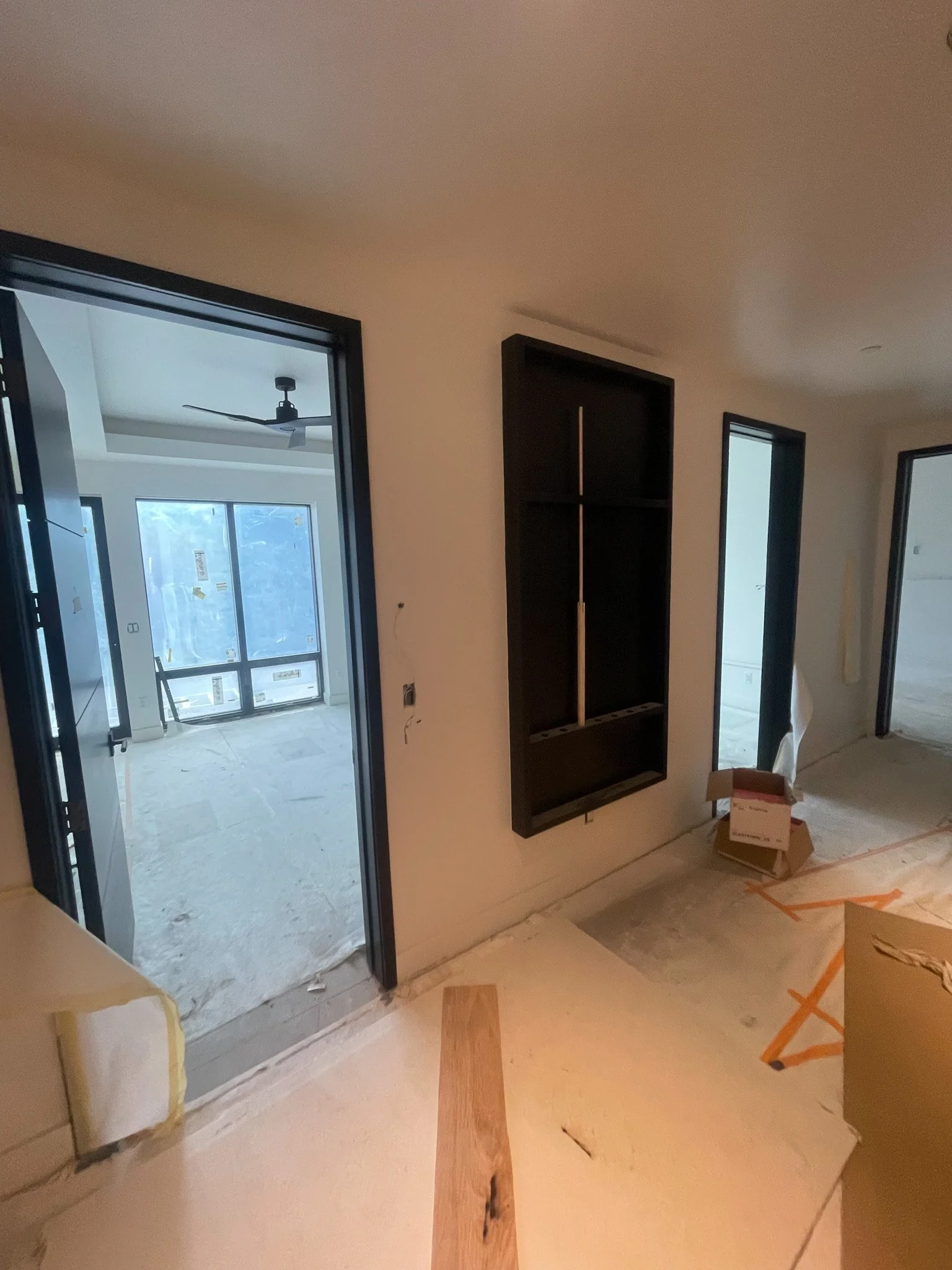 Interior view of a room under construction with multiple doorways and a black shelving unit on the wall, with construction materials and packaging on the floor.