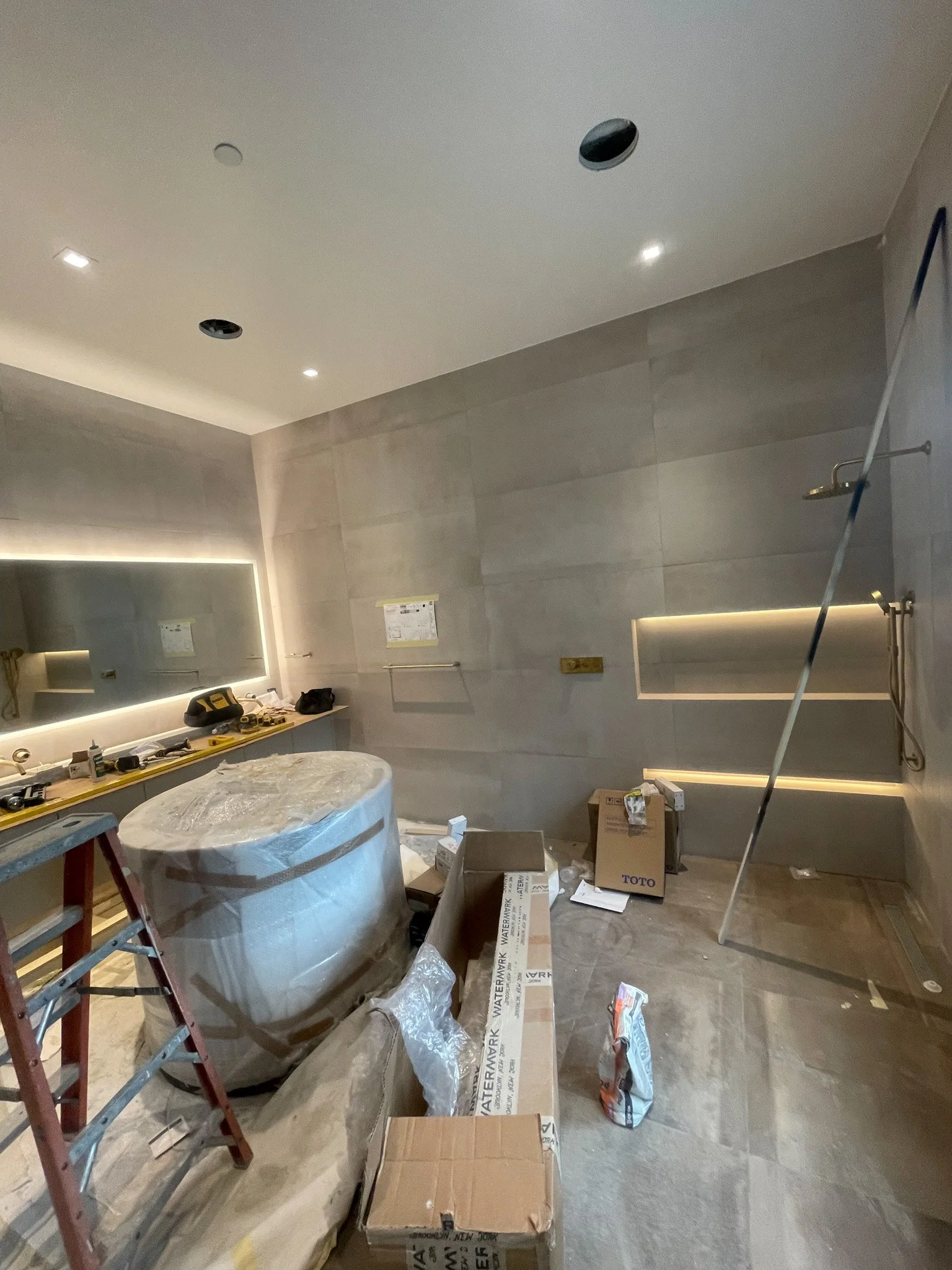 Interior under construction with tools, boxes, and a wrapped bathtub in a partially finished bathroom.