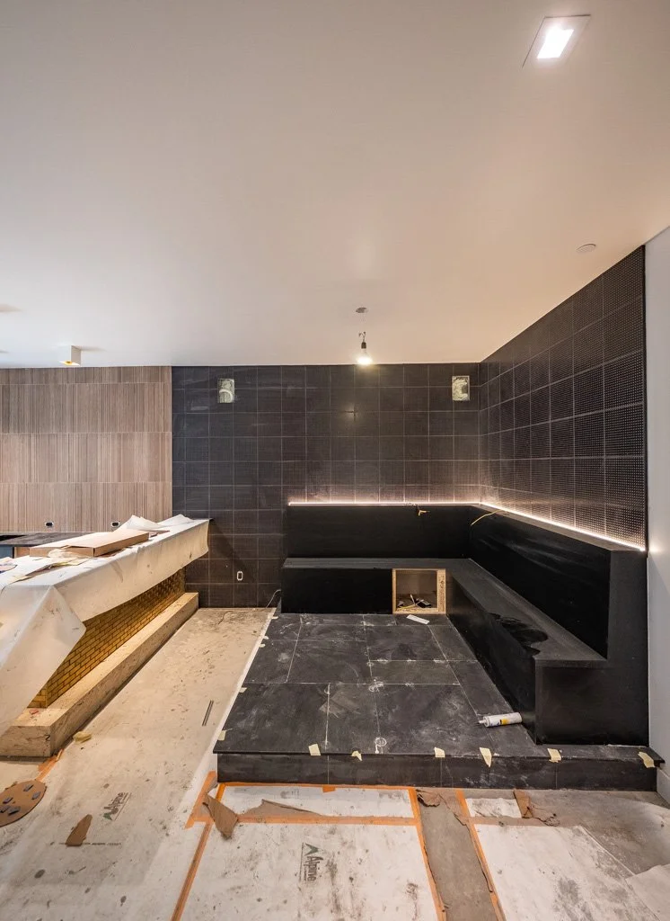 Interior of a room under construction with black tiled walls, a built-in black seating area, and construction materials on the floor.