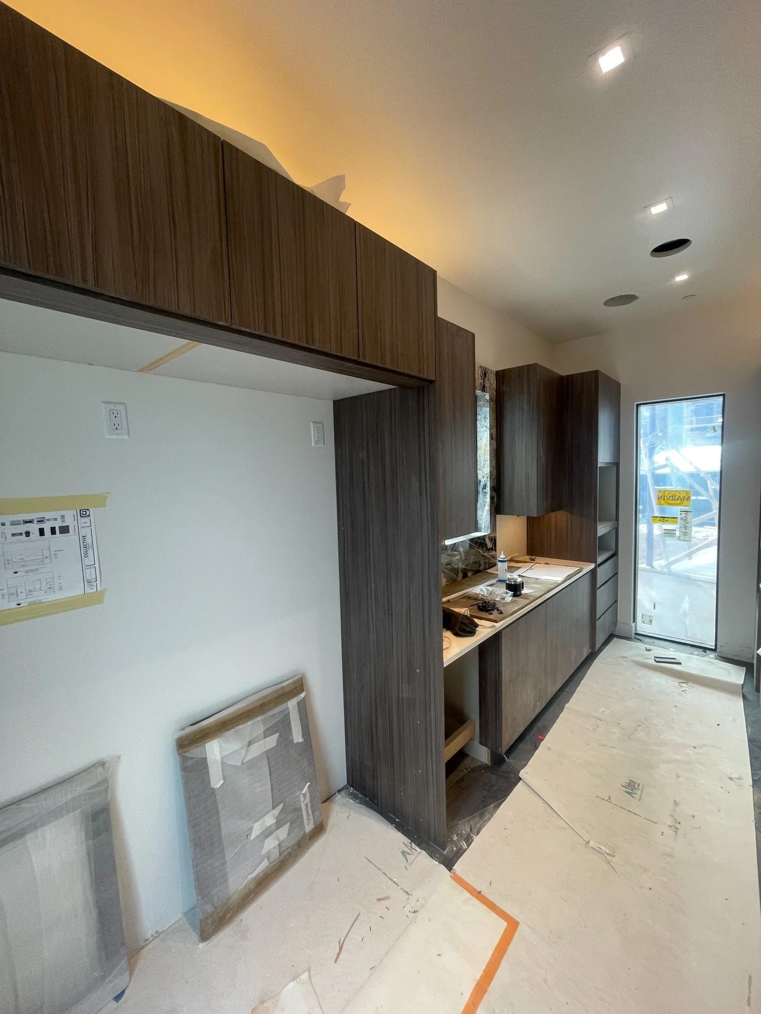 Interior of a kitchen under construction with dark wood cabinets, construction materials, and a door leading outside.