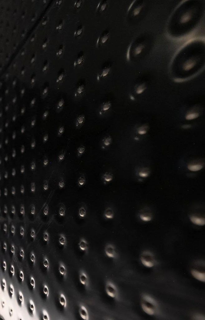 Close-up of a metallic surface with numerous small circular holes arranged in a pattern.