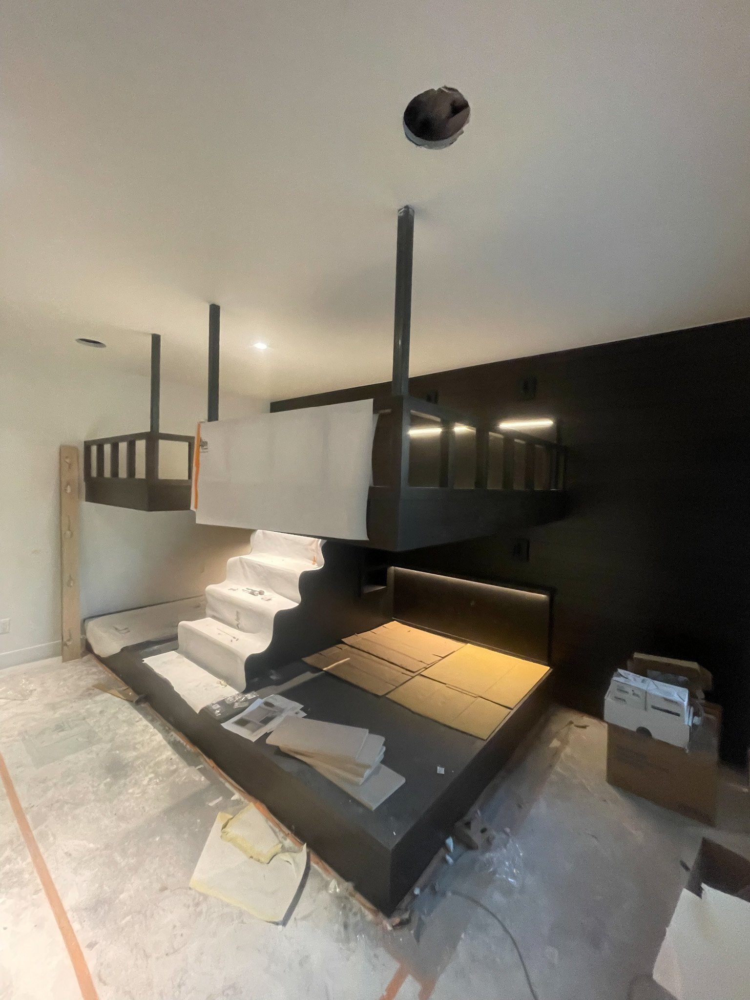 Construction site with black stairs and a balcony, indicating ongoing interior renovation or assembly.