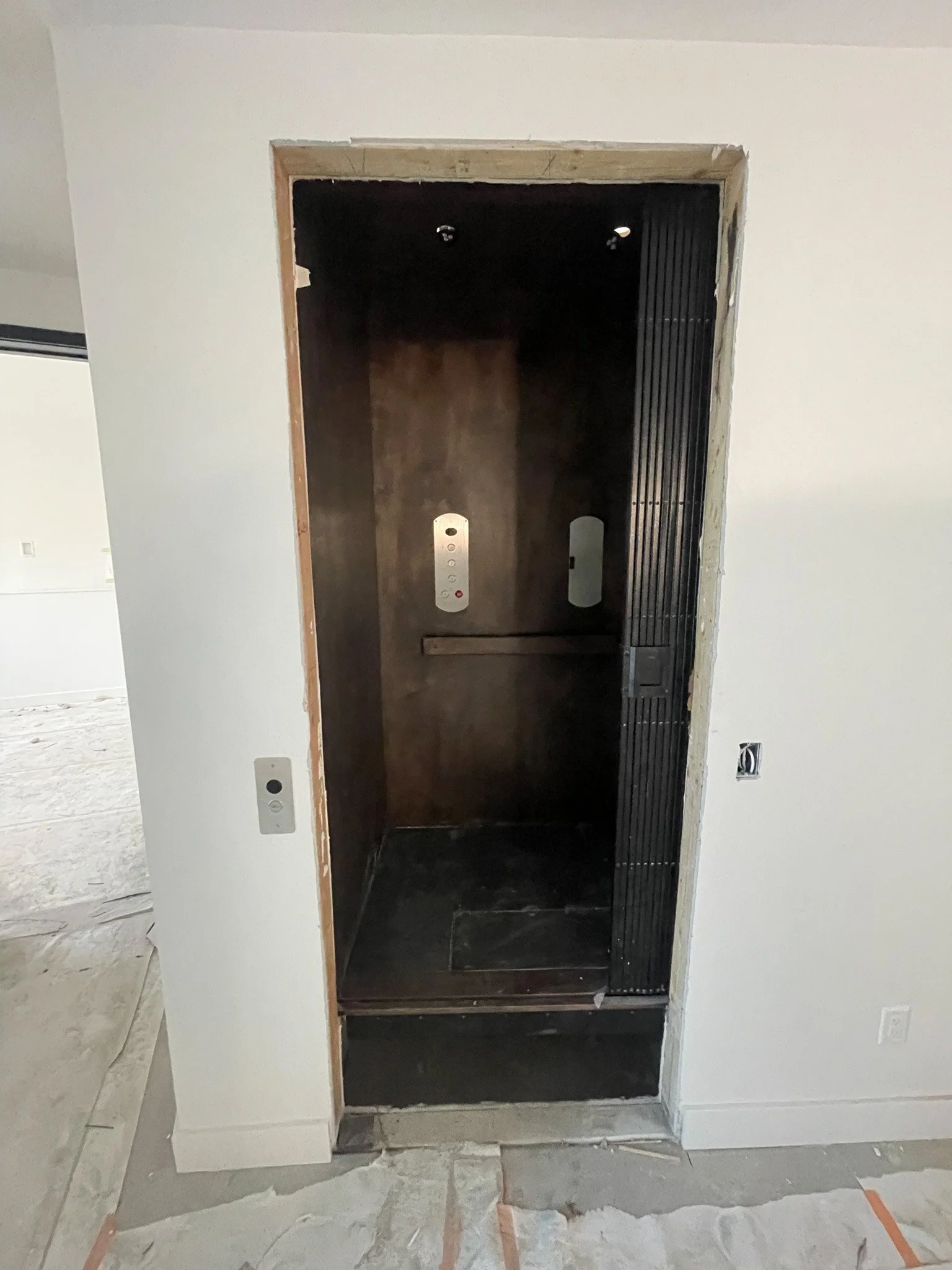 Empty elevator cab with dark interior, wooden walls, and minimal lighting, under construction or renovation.