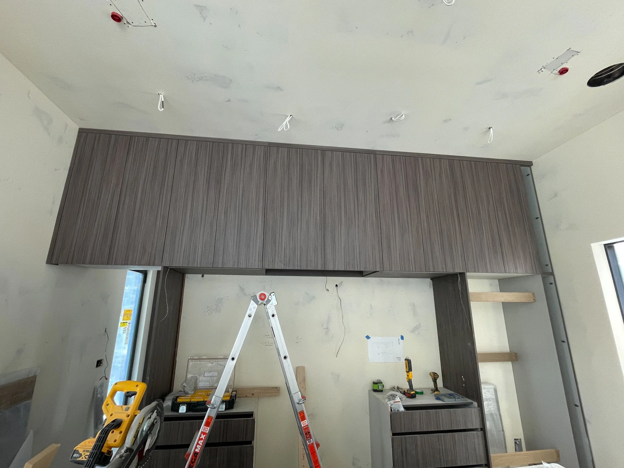 Interior of a room under renovation with a wooden cabinet, a ladder, and various tools on the countertop.