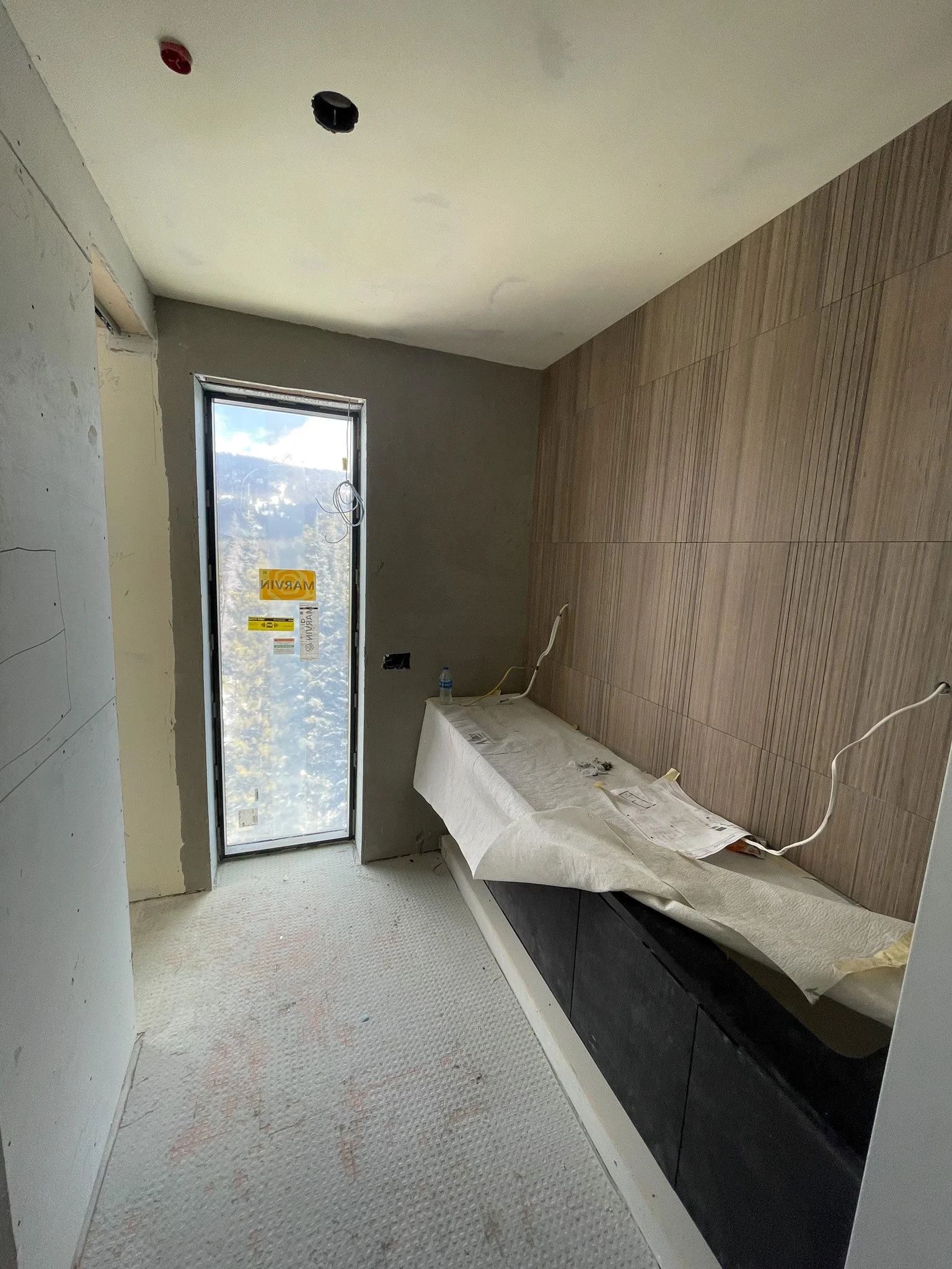Bathroom under construction with a window, wooden wall panels, and black cabinets covered with protective paper.