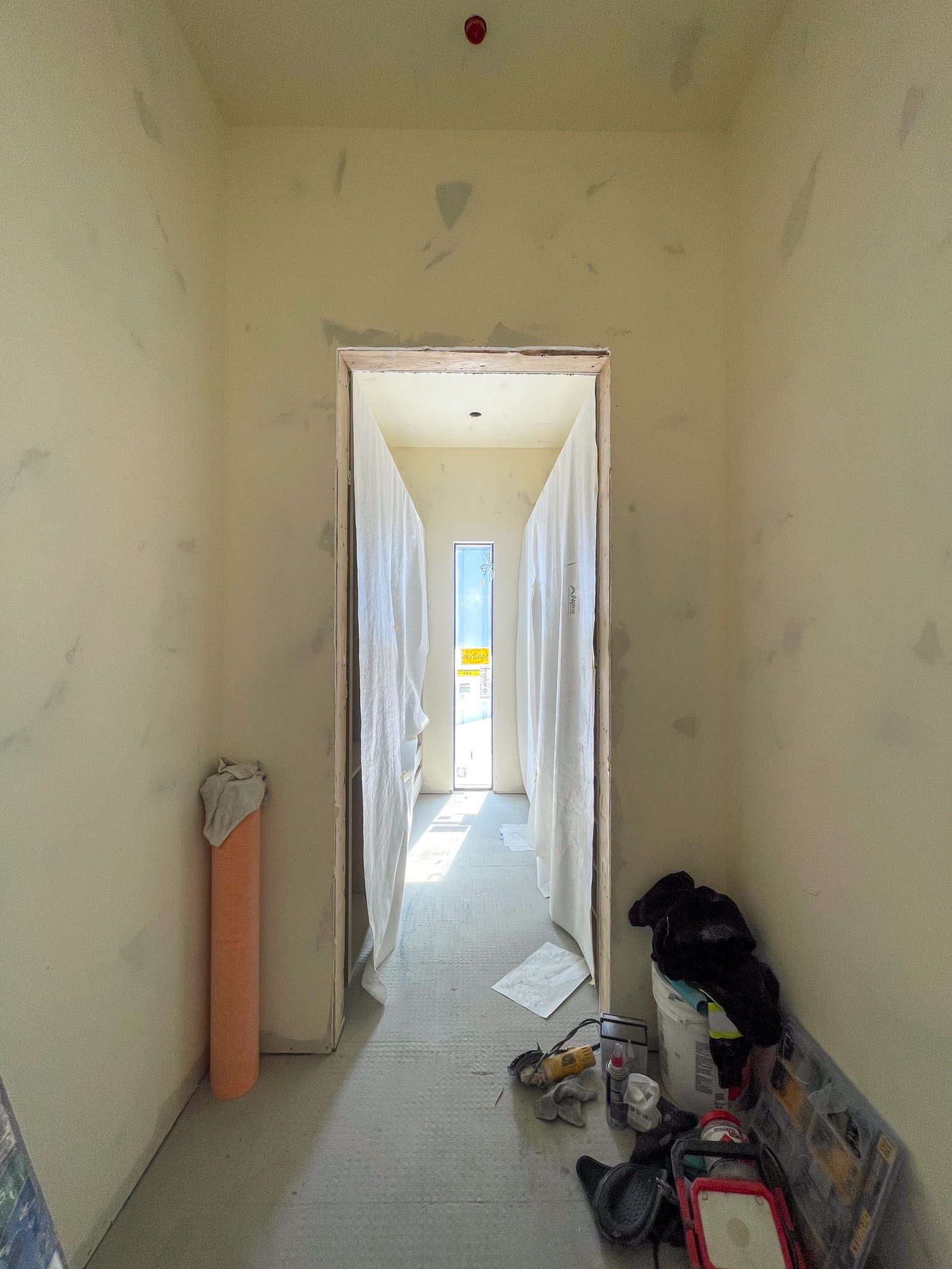 Interior of a construction site with unfinished drywall, tools, and supplies on the floor.
