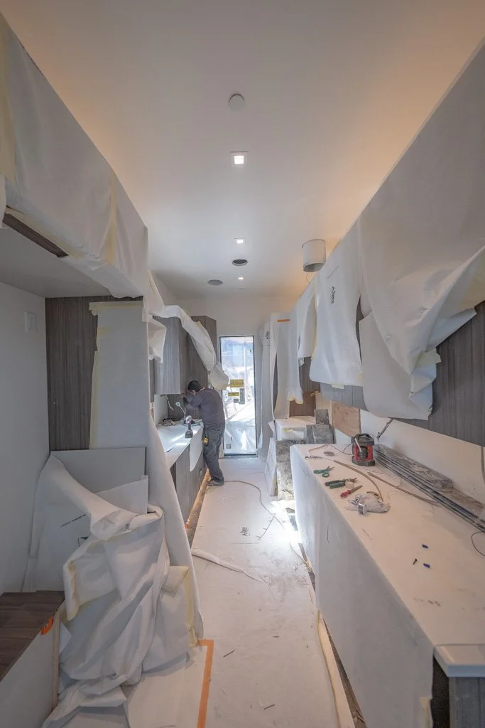 Construction workers installing or renovating a kitchen, with protective sheets hanging and tools on the counter.