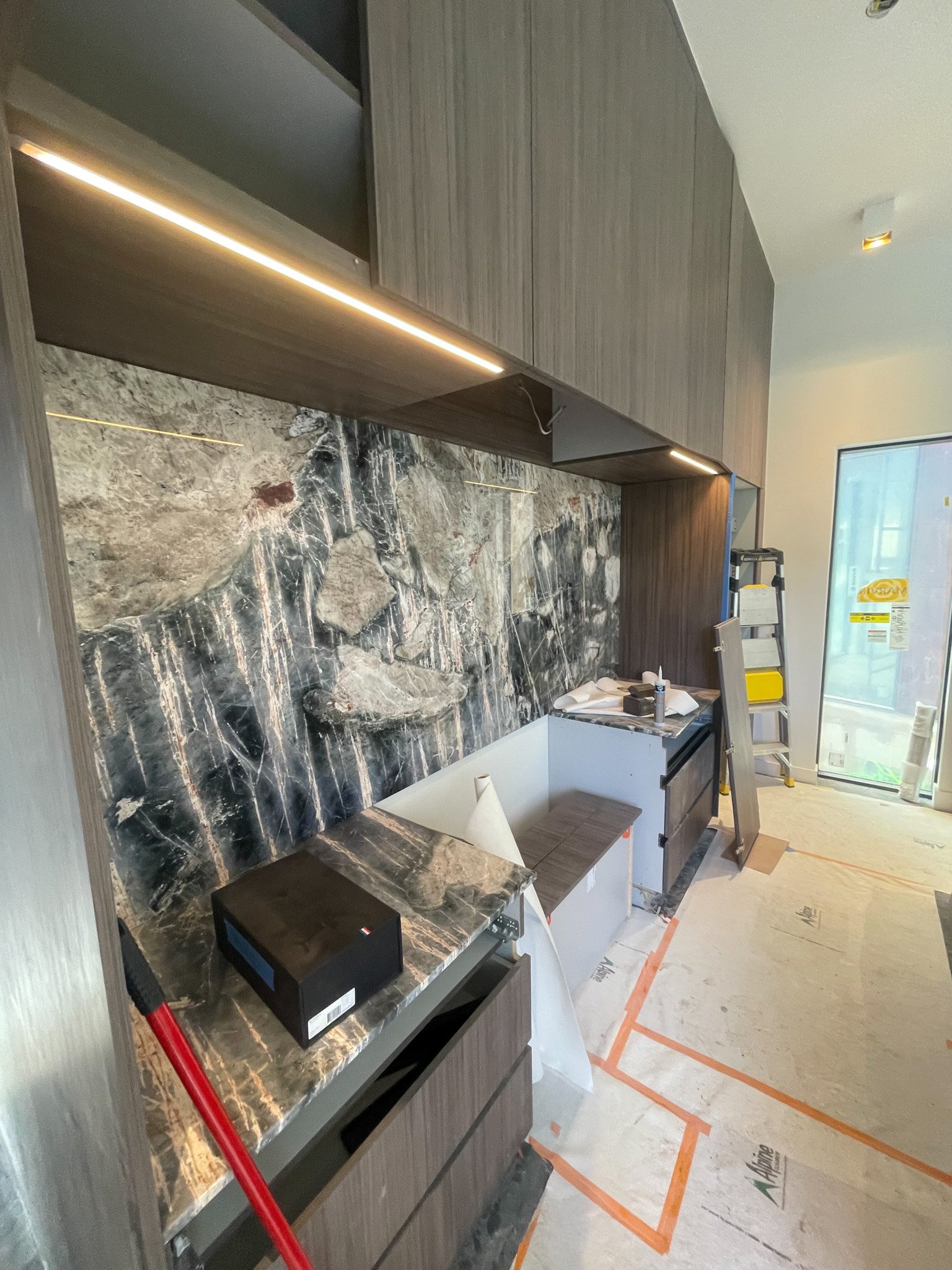 Construction site of a kitchen with dark wood cabinets, black and gold marble backsplash, and a glass door entrance.