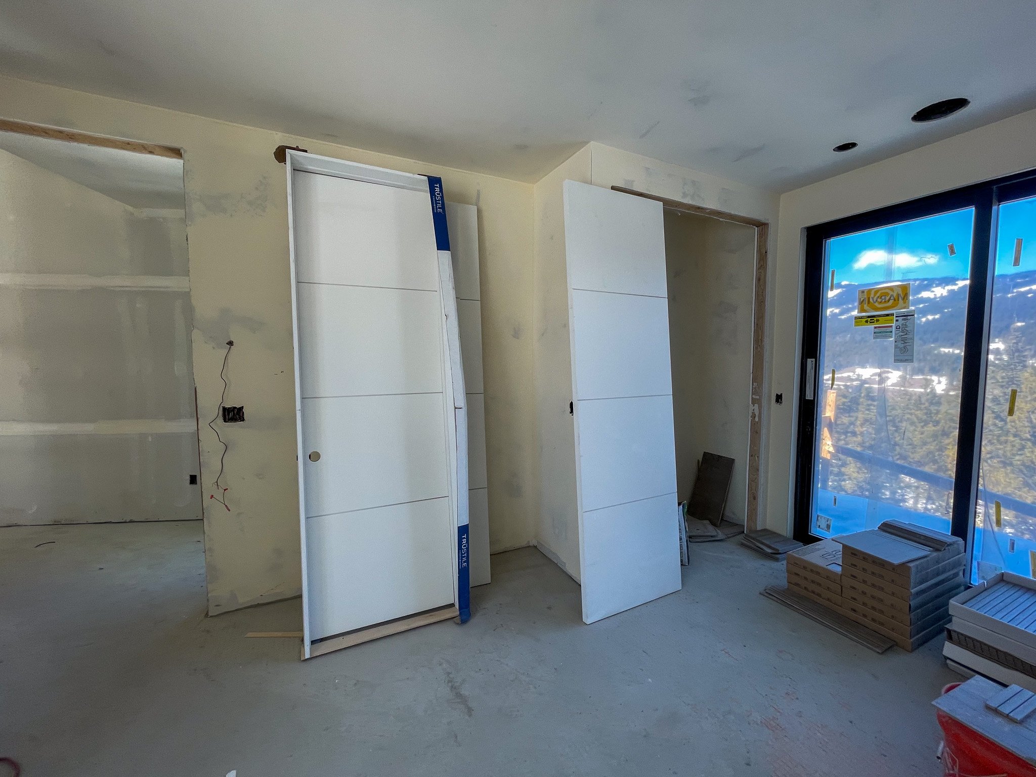 Interior view of a room under construction with drywall, construction materials, and a glass sliding door.