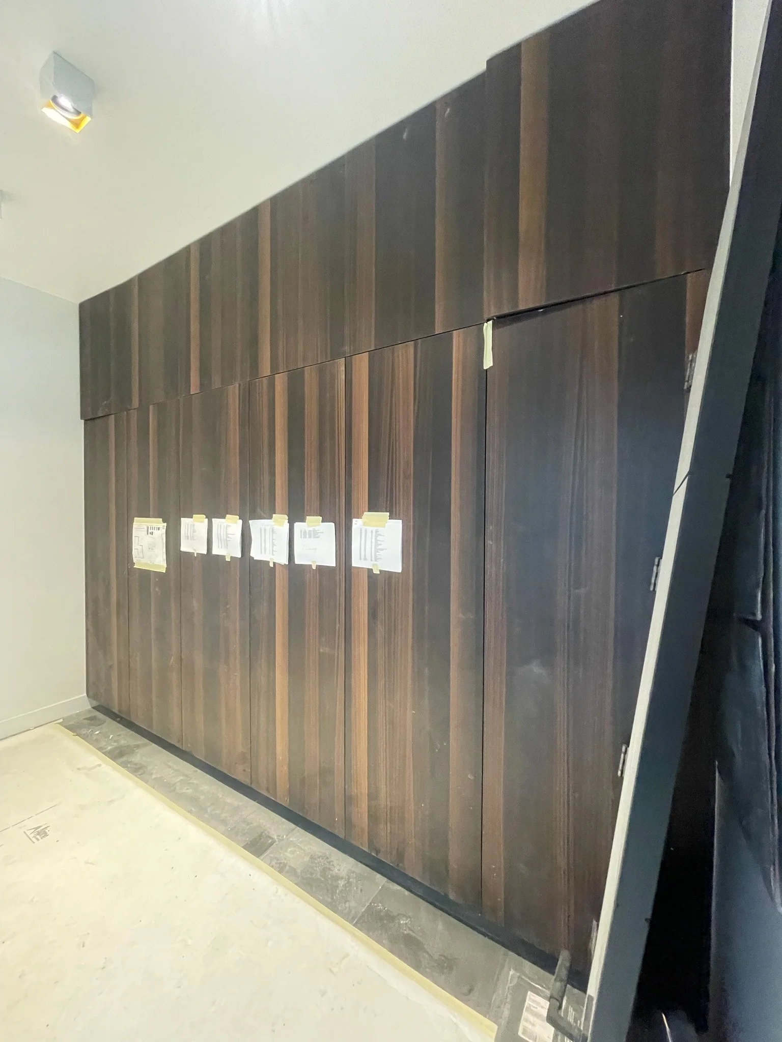 Dark wooden cabinetry being installed in a room with some paper notes taped to the doors