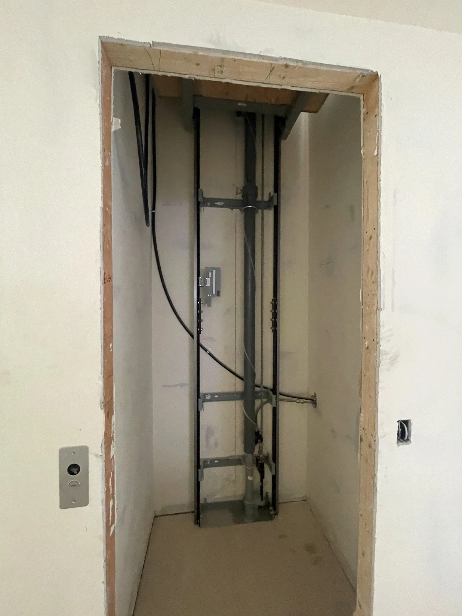 An unfinished room with exposed plumbing and electrical wiring in the wall, with the opening for a closet or small utility space.