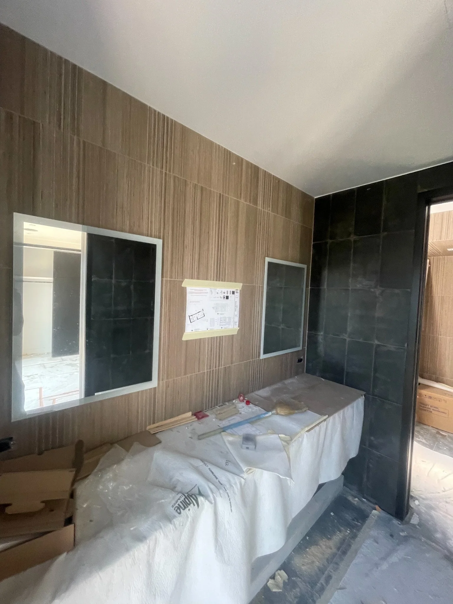 Construction site inside a building with framed mirrors and protective coverings, with construction tools and materials on a table.