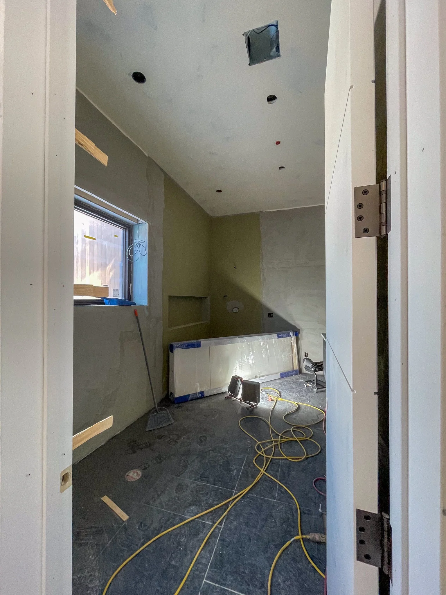 Room under construction with drywall, a window, electrical outlets, wiring, and construction tools on the floor.