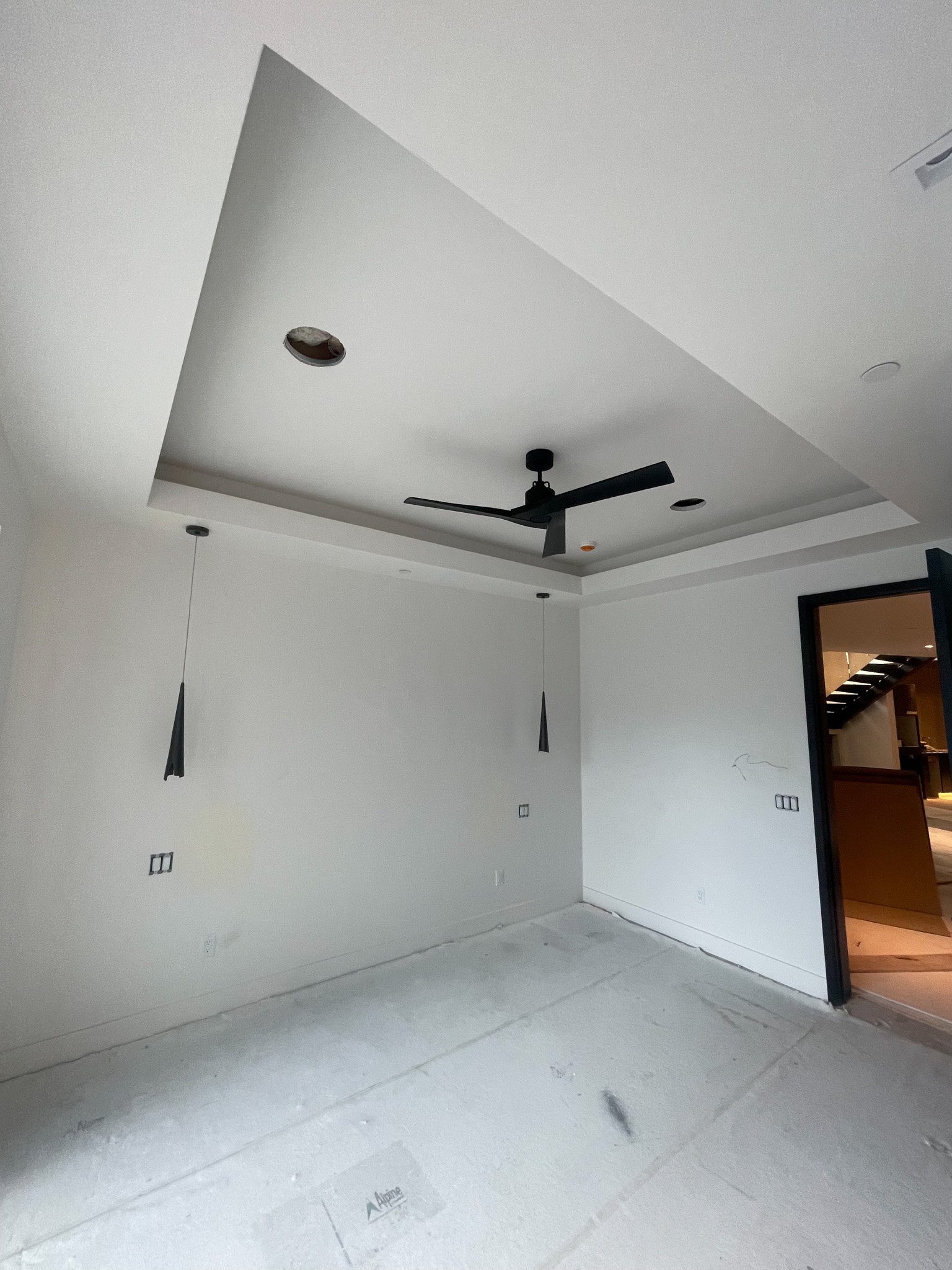 Empty room under construction with a ceiling fan, pendant lights, and a doorway leading to another room.