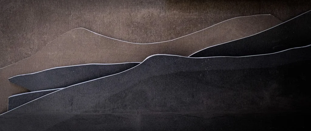 Abstract paper cut-out shapes resembling mountain ranges in shades of brown, black, and gray.