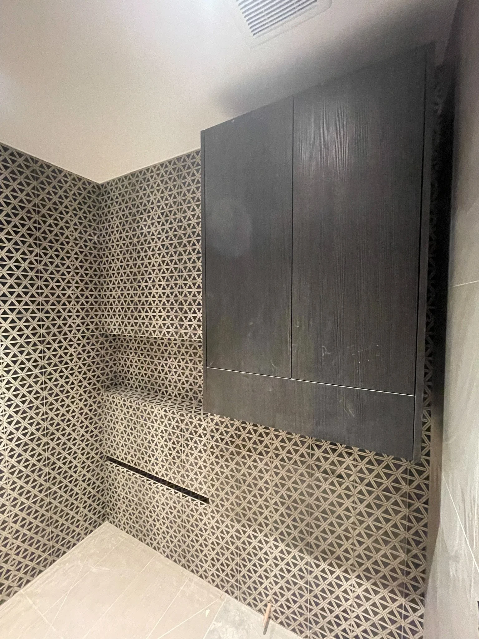 A bathroom corner with geometric patterned tiles on the walls and a black wooden cabinet above the floor.