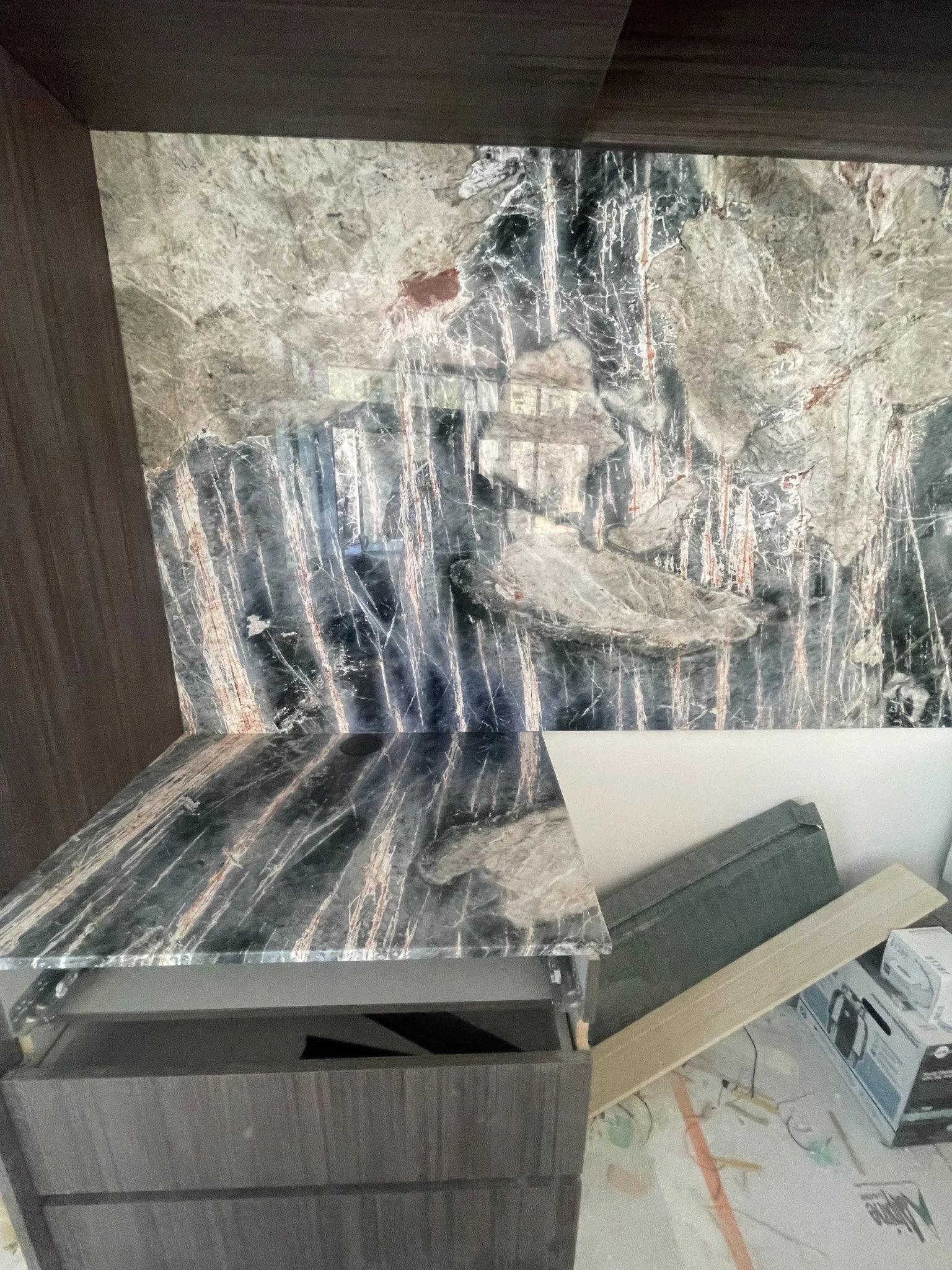 Close-up of a marble countertop and backsplash with a dark veined pattern, part of a kitchen under construction, with construction materials and tools visible below.