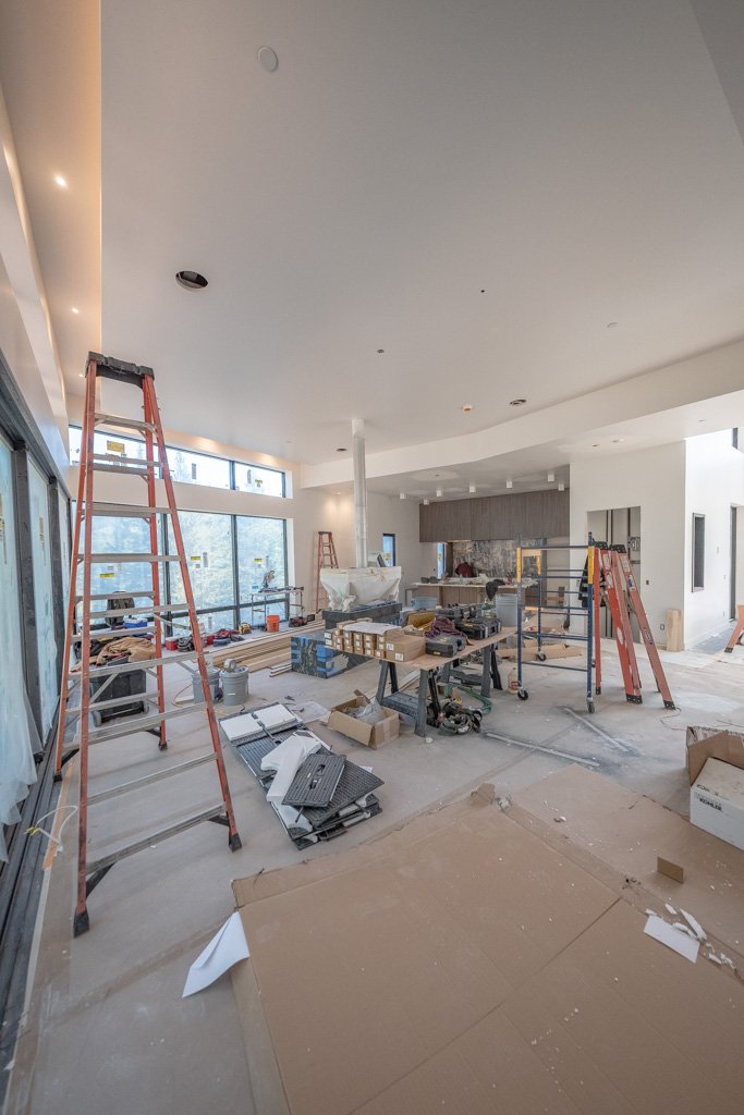 Interior of a house under construction with ladders, tools, and construction materials scattered across the floor.