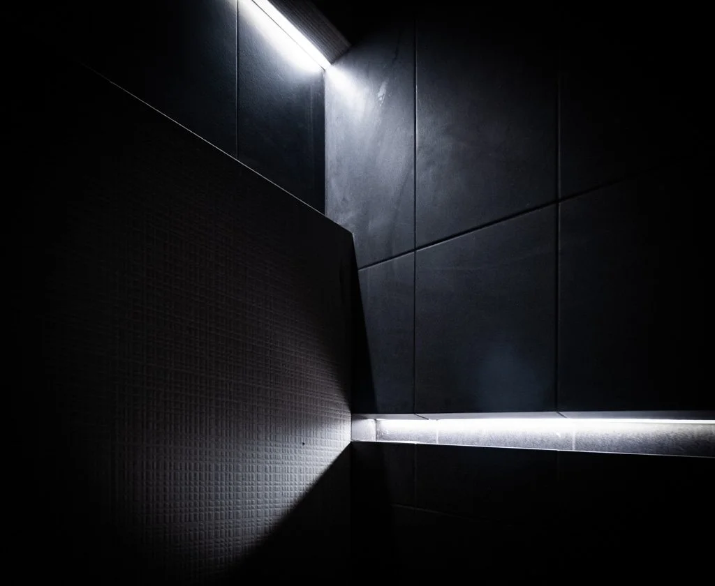 Dark tiled wall with a bright LED strip light running along the edge, creating contrasting shadows and highlights.