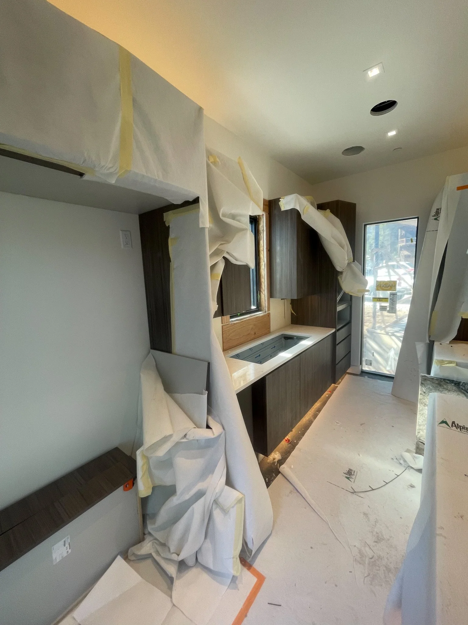 Kitchen under construction with cabinets, countertops, and protective coverings on surfaces.