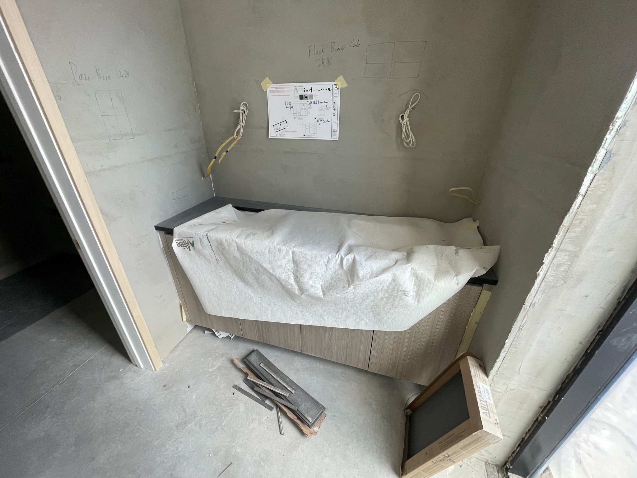 Small construction or medical room with a countertop and a covered sink, electrical wiring and outlets on the wall, and construction tools on the floor.