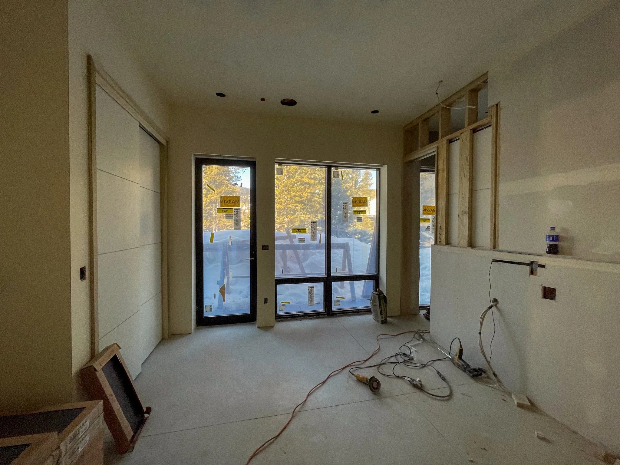 Interior of a room under construction with large windows and construction tools on the floor.