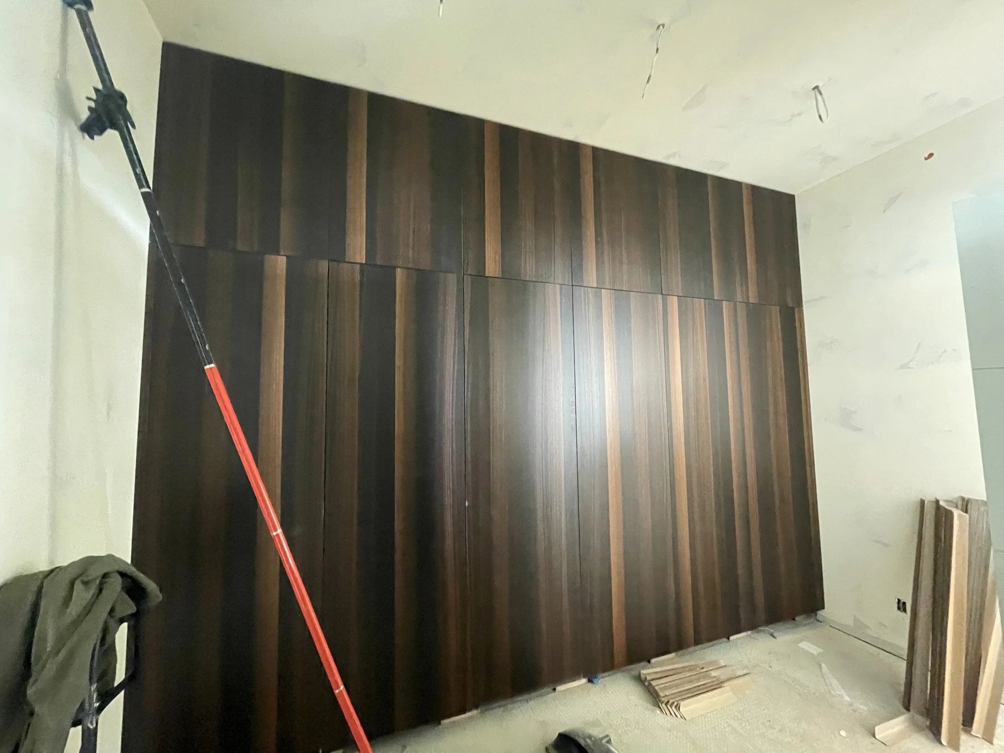 A large dark wood panel wall in a room under construction, with construction tools and materials visible on the floor and a drying mop leaning against the wall.