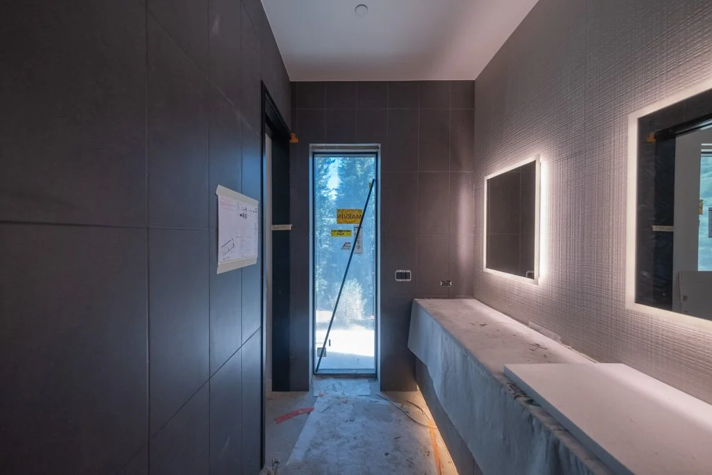 Interior of a modern room under construction with dark wall tiles, a window, and backlit mirror.