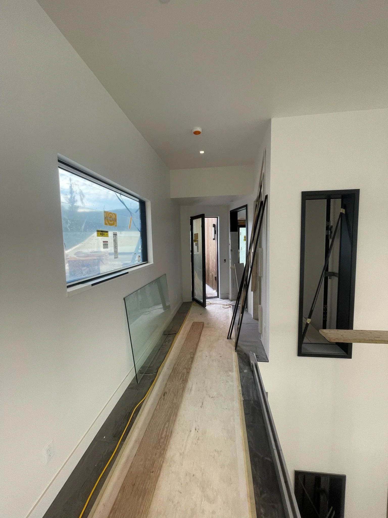 Interior of a house under construction with a long hallway, large window, and various construction materials and tools.