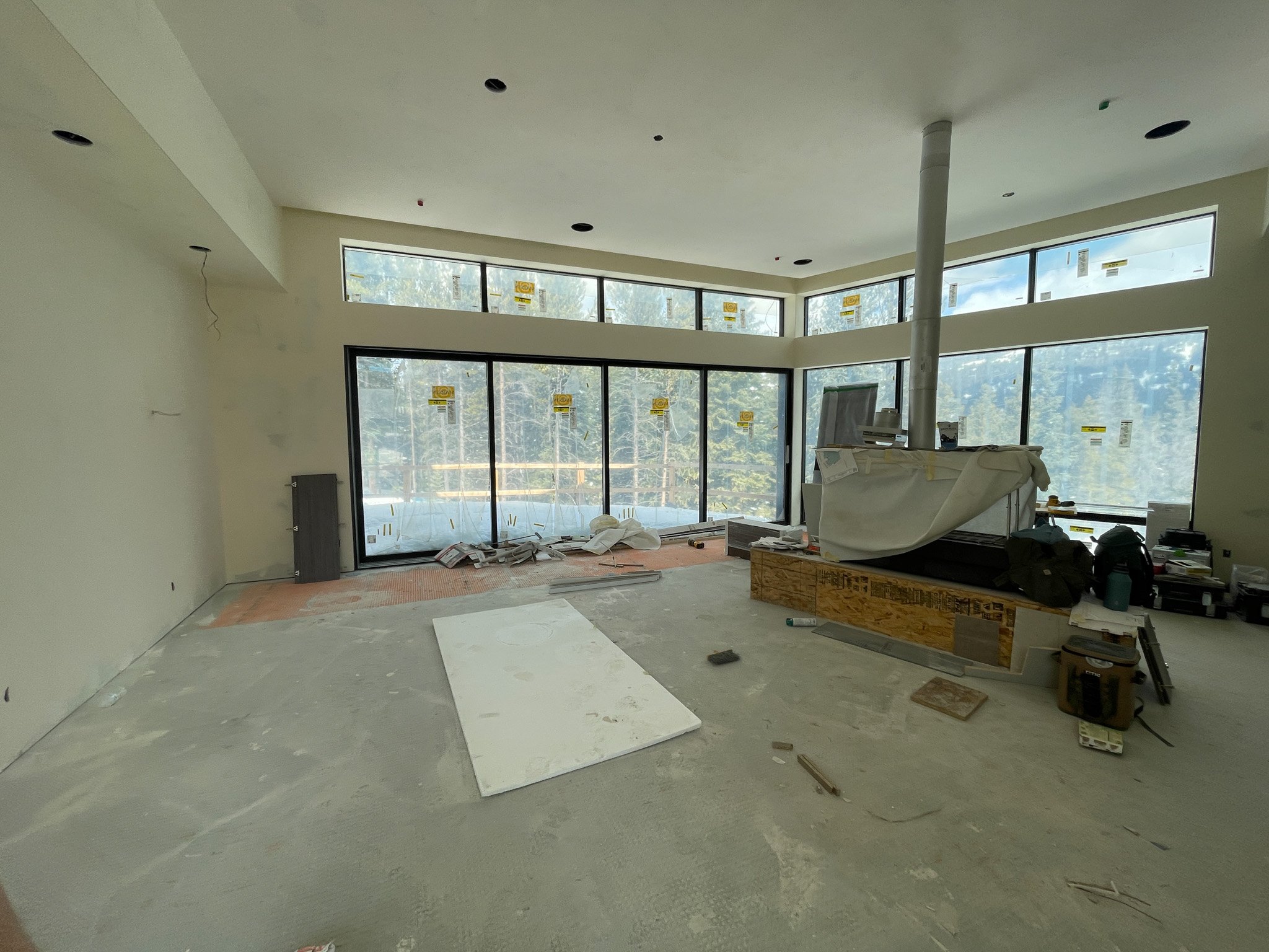 Interior of a room under construction with large windows, construction materials, and tools scattered on the floor.