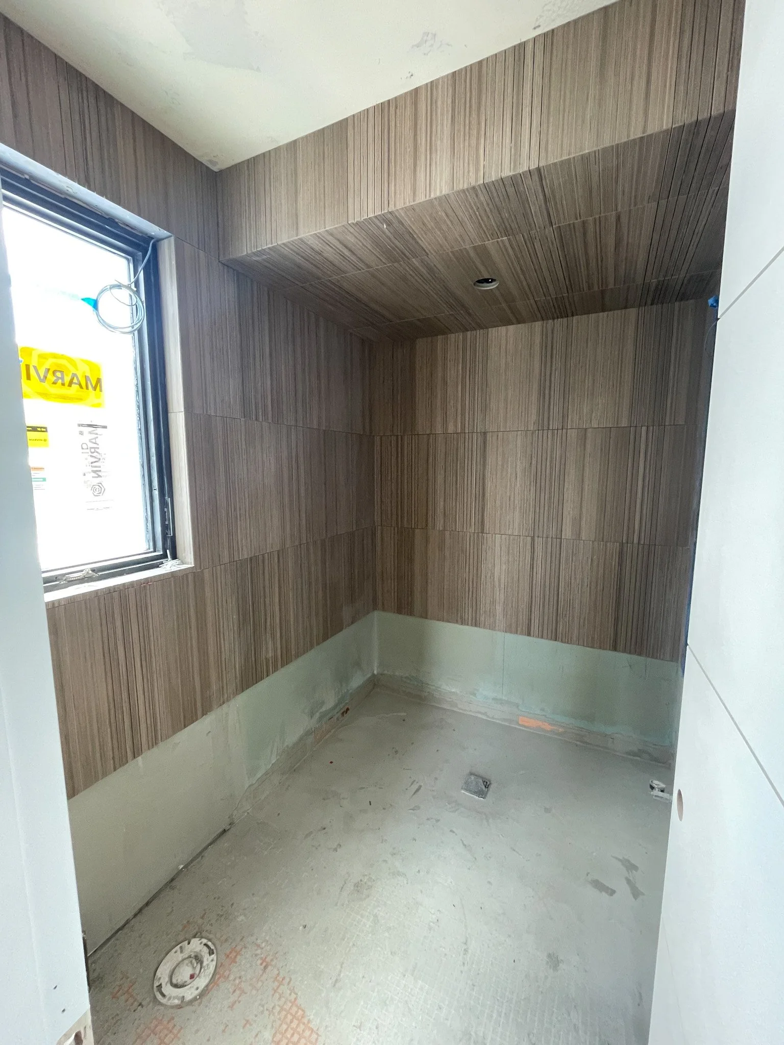 Empty room under construction with brown tiled walls, a small window, and a concrete floor with plumbing fixtures.
