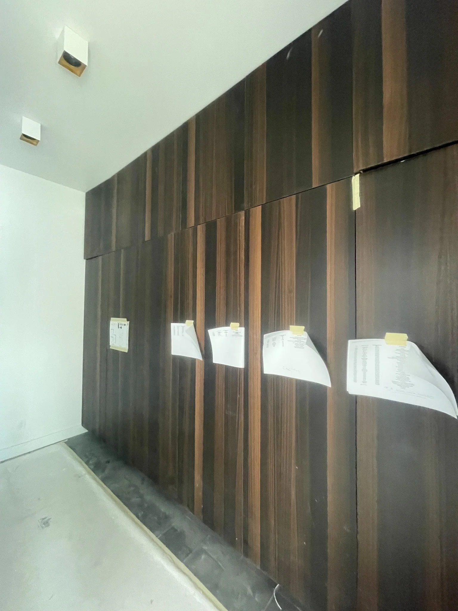 A wooden wall with papers taped to it, in a room under construction or renovation.