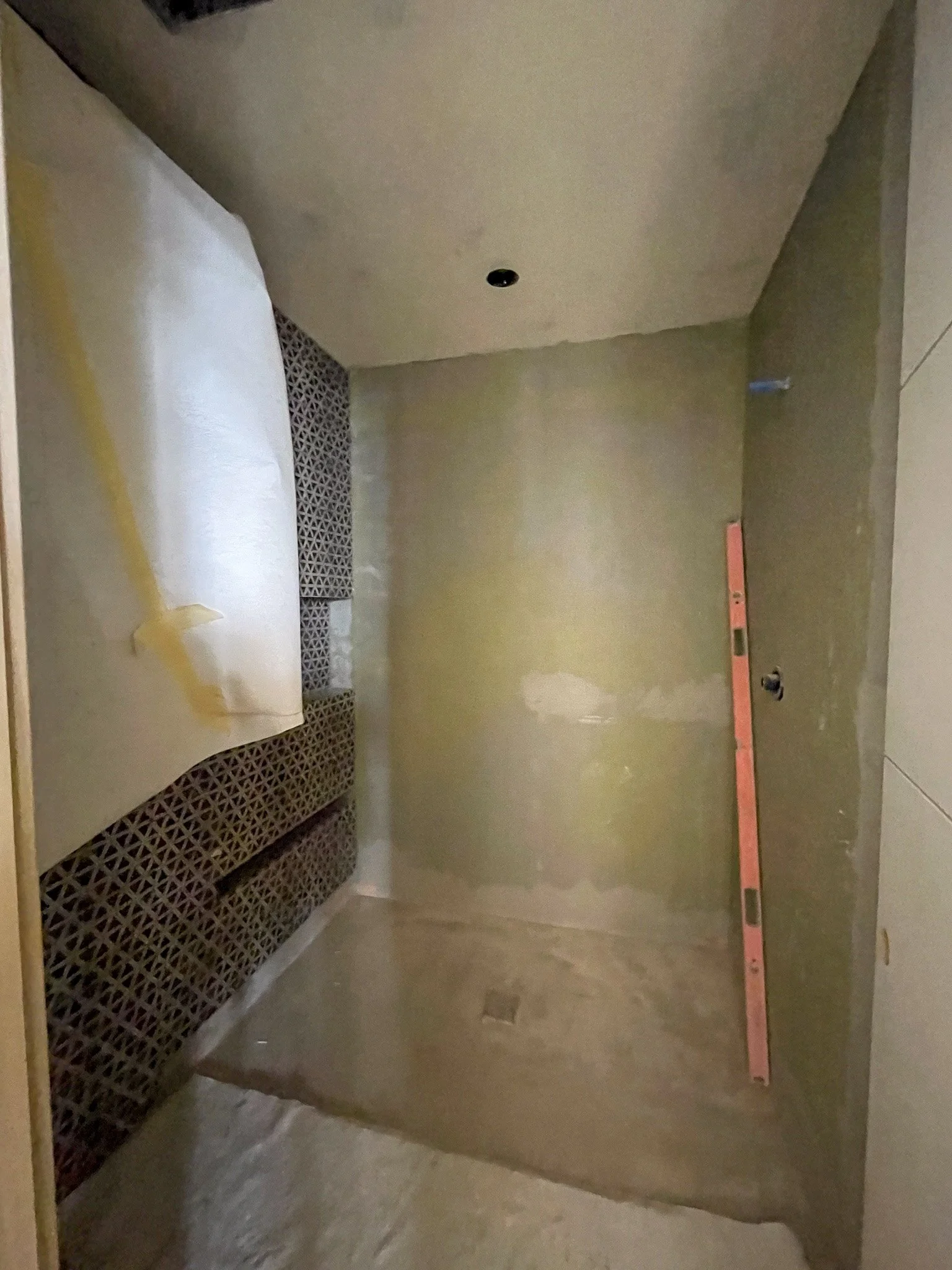 A small room under construction with green drywall, a black patterned tile feature, a level propped against the wall, and a partially covered window.
