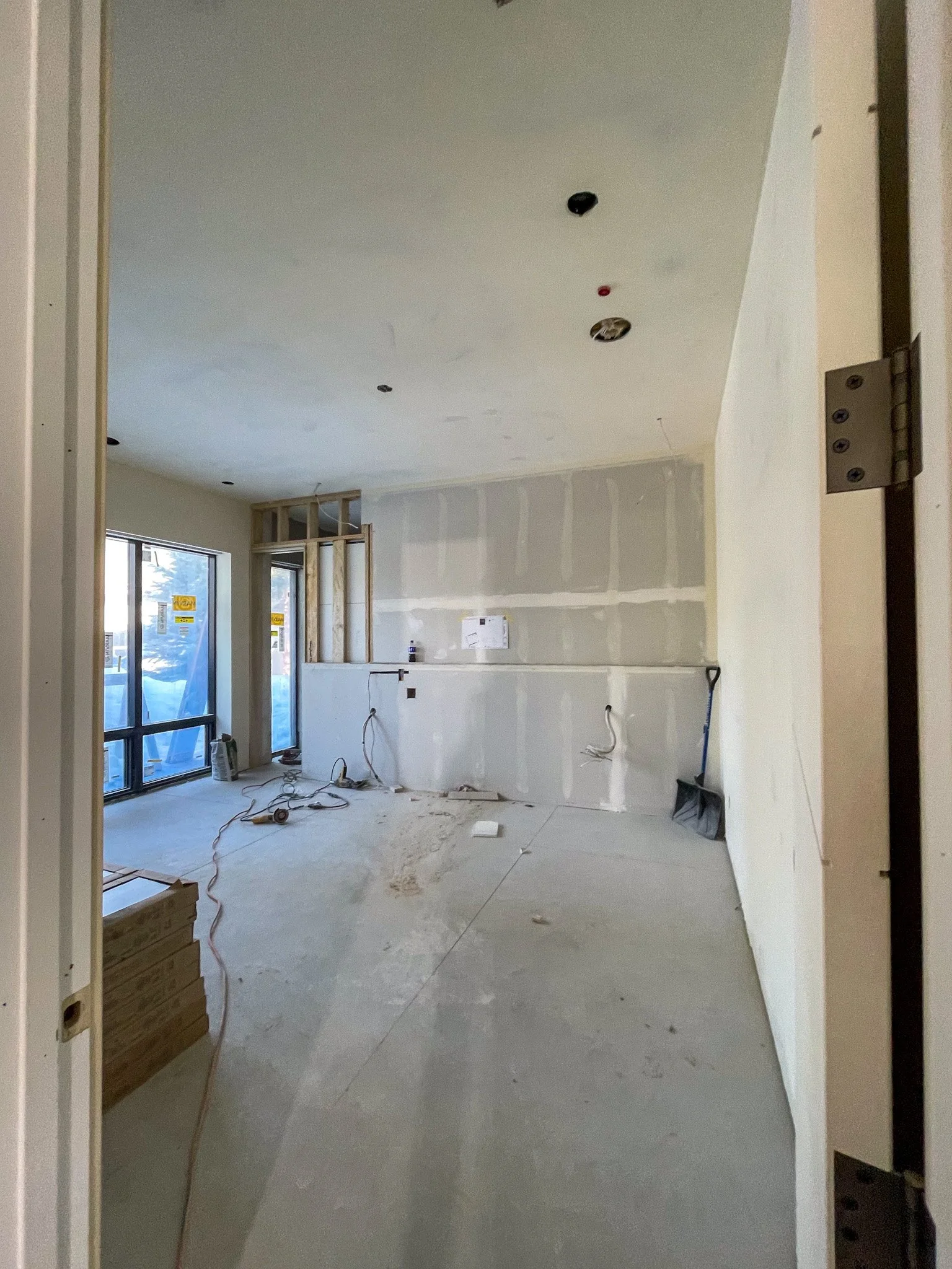 Interior of a room under construction with drywall, unfinished walls, and some construction tools and materials on the floor.