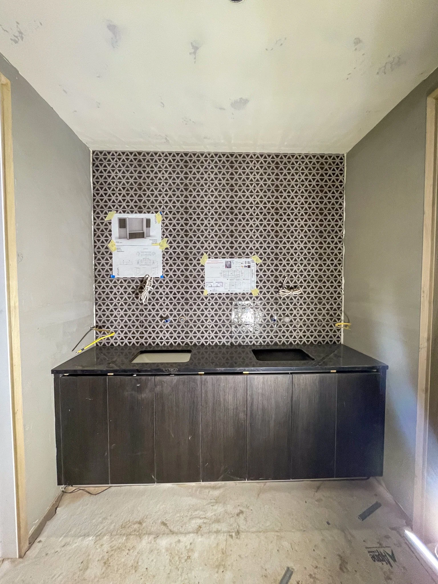 Kitchen under construction with a black countertop, a geometric patterned backsplash, and an unfinished wall and floor.