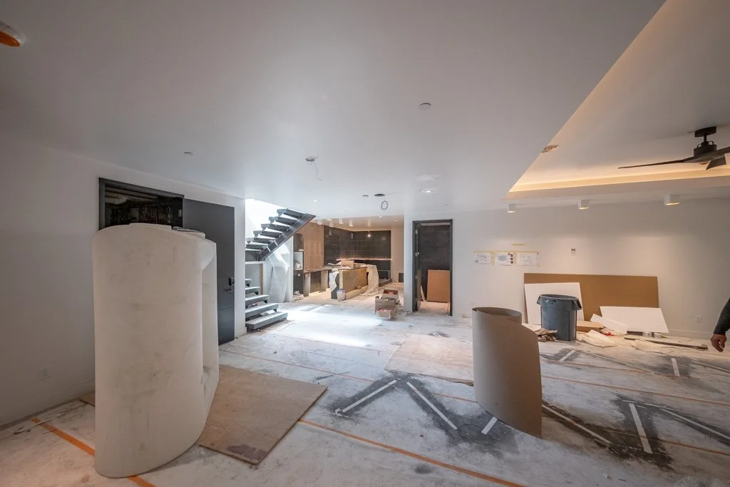Interior of a room under construction or renovation with construction materials and tools scattered around, a staircase, and an illuminated false ceiling.