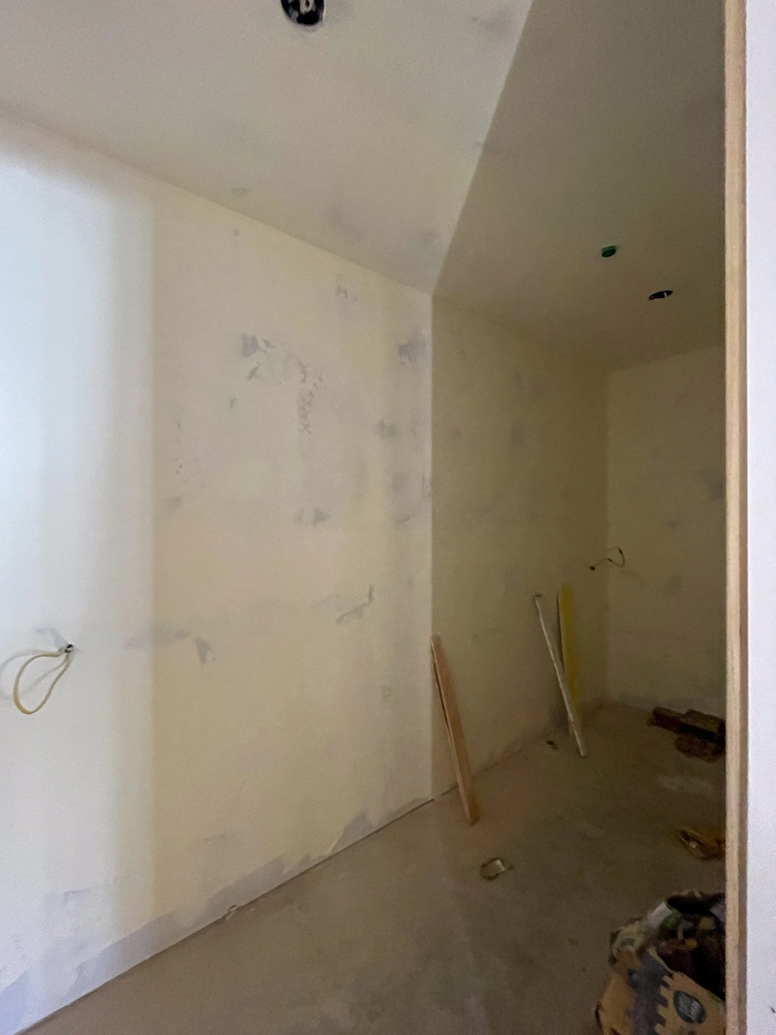 An unfinished room under construction with drywall partially installed, visible electrical wiring, and construction materials on the floor.