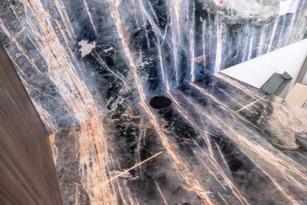 Close-up of a black marble countertop and backsplash with orange and white veins, featuring a circular black drain cover in the center.